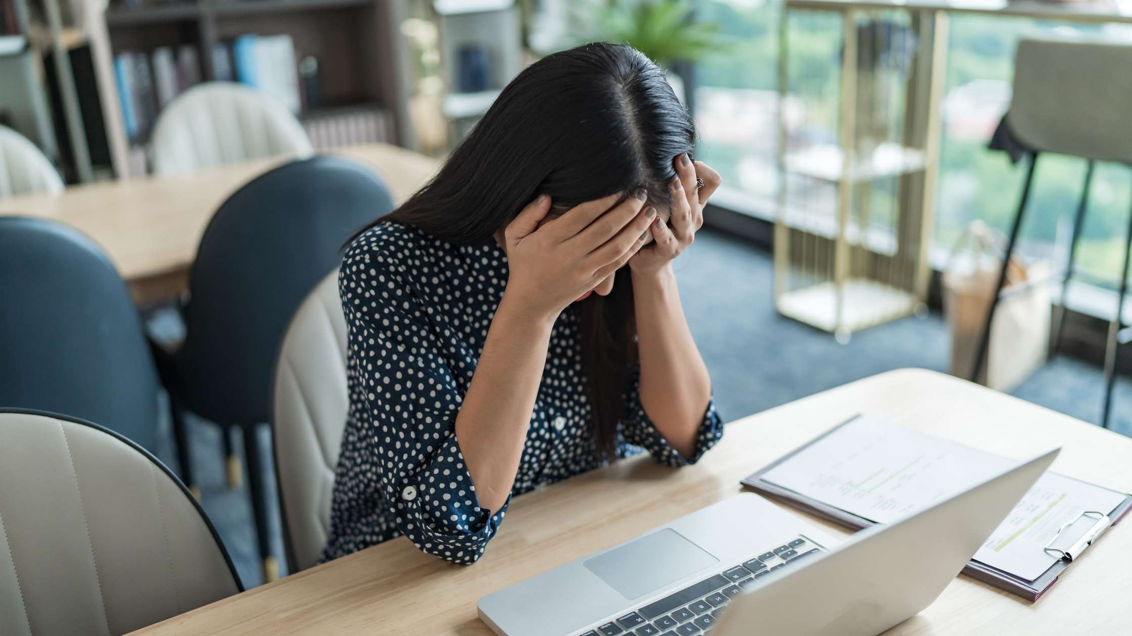 Mulher branca setada em uma mesa, em frente ao computador, triste/esgotada